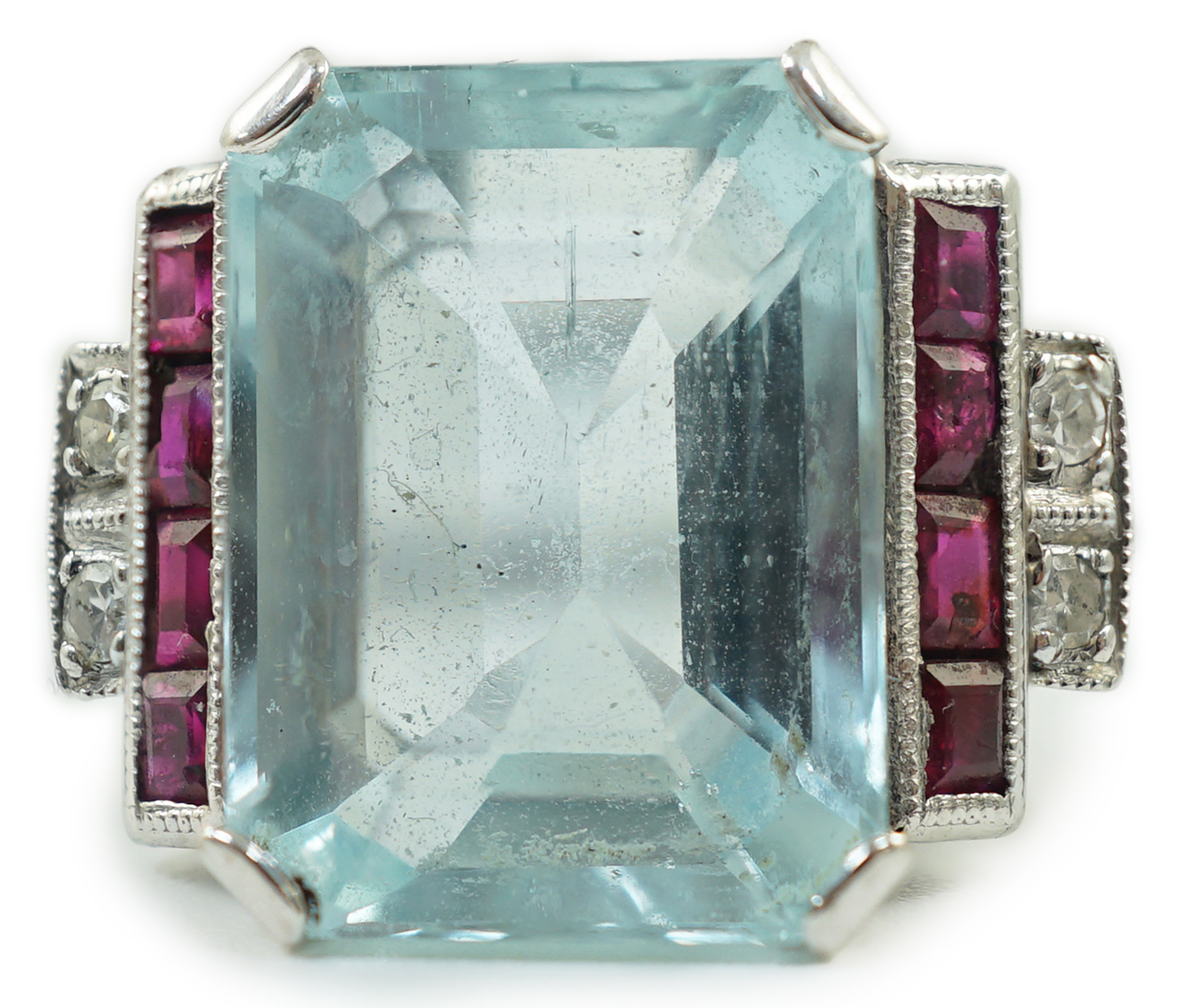 A platinum and single stone emerald cut aquamarine set dress ring, with ruby and diamond set stepped shoulders